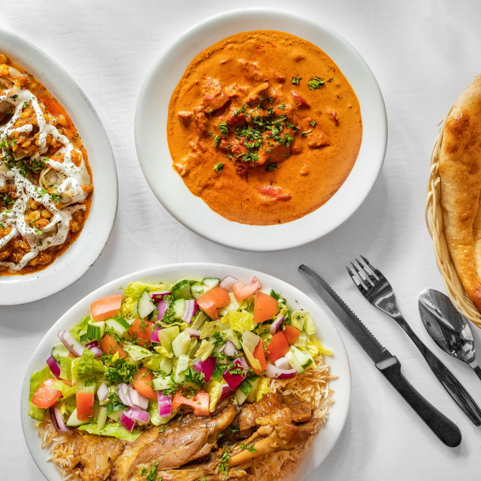 Butter chicken, kabobs over Afghan rice and salad on a white table